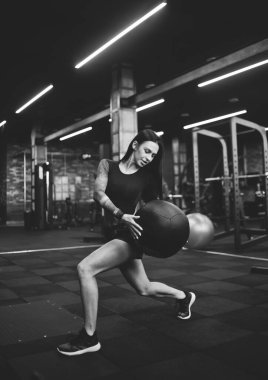 Spor kıyafetli, sağlıklı bir kadın spor salonunda tıp topuyla egzersiz yapıyor. Siyah beyaz fotoğraf