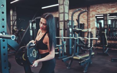 Sportif esmer kadın halter için ağırlık diskini spor arka planına koyuyor.