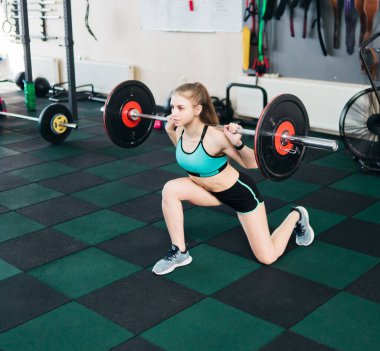 Genç, formda bir kadın spor salonunda halterle bacaklarına atlıyor.