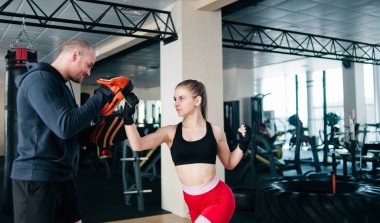 Sarışın kadın, erkek antrenörle yumruk antrenmanı yapıyor. Spor salonunda. Yumruk atan çift