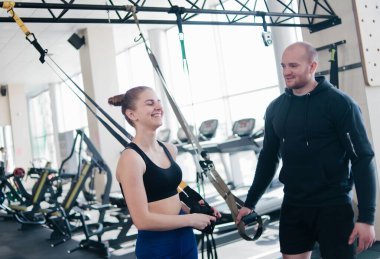 Formda bir kadın ve erkek egzersize ara verirken spor kayışlarıyla konuşuyor.