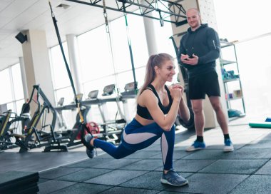 Kişisel bir eğitmenin gözetiminde eğitim. İşlevsel eğitim. Spor salonunda kemerleriyle egzersiz yapan bir kadın.