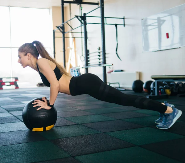 Athletic attractive woman doing push up exercise with medicine ball. Functional training
