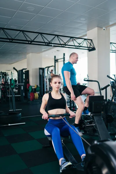 Functional training concept. Sport man and woman doing exercise in  simulator rowing machine and air bike at gym