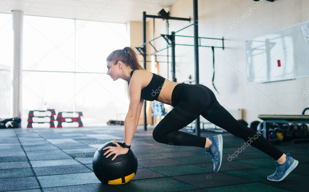 Athletic attractive woman doing an exercise lifting the leg up leaning on the medicine ball. Functional training concept