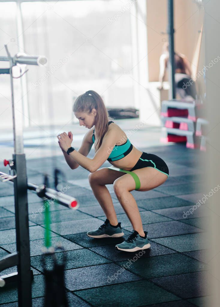 Young fit woman doing squats with a rubber band in the gym. Functional modern training