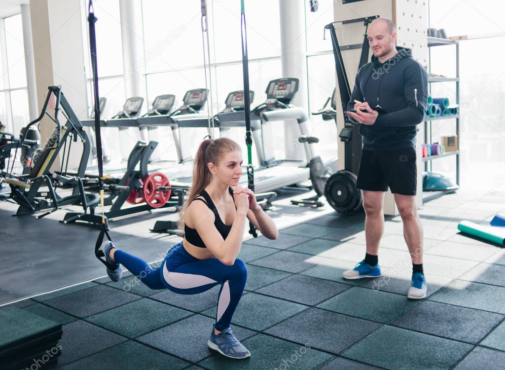 Training under the supervision of a personal trainer. Functional training. Woman doing exercise with futness straps in the gym