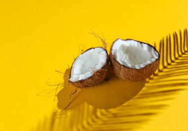 Minimalist tropikal natürmort. Sarı arka planda palmiye yapraklarının gölgeleriyle iki parça doğranmış hindistan cevizi. Yaratıcı moda kavramı.