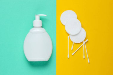 Minimalist güzellik konsepti. Şişe kremi, pamuk pedler, mavi-sarı arka planda kulak çubukları. Üst görünüm
