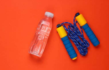 Düz yatış tarzı spor konsepti. İp atlama, bir şişe su. Turuncu arka planda spor malzemeleri. Üst görünüm