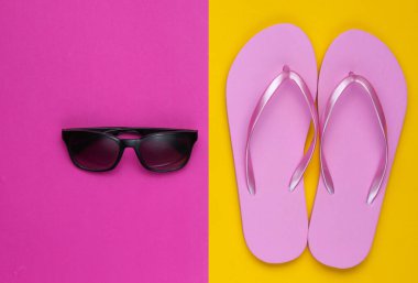 Yaz hala hayattır. Plaj aksesuarları. Havalı plaj pembe terlikleri, renkli kağıt arka planda güneş gözlüğü. Düz yatıyordu. Üst görünüm