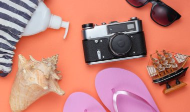 Yaz hala hayattır. Plaj aksesuarları. Moda pembe terlikler, çanta, retro kamera, güneş kremi şişesi, güneş gözlüğü, mercan kağıdında deniz kabuğu. Düz yatıyordu. Uzayı kopyala Üst görünüm