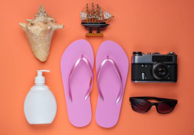 Yaz hala hayattır. Plaj aksesuarları. Moda pembe parmak arası terlikler, retro kamera, güneş kremi şişesi, güneş gözlüğü, mercan kağıdında deniz kabuğu. Düz yatıyordu. Üst görünüm