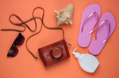 Yaz hala hayattır. Plaj aksesuarları. Moda pembe parmak arası terlikler, retro kamera, güneş kremi şişesi, güneş gözlüğü, mercan kağıdında deniz kabuğu. Düz yatıyordu. Üst görünüm