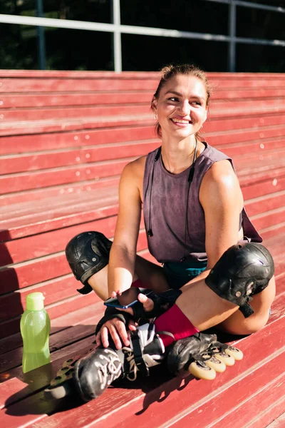 Cheerful sporty woman roller skating in roller skates sitting on a wooden tribune on the sports ground