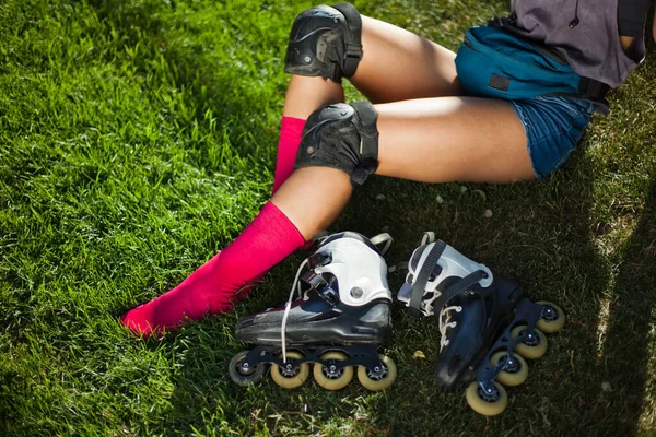 Female legs in pink long socks and roller skates are sitting on the grass lawn.