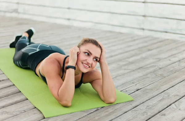 Slim woman training on yoga mat on wooden promenade Stock Photo by