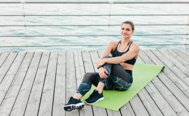 Spor giyimli genç kaslı kadın plaj terasında minderde otururken dinleniyor. Sağlıklı yaşam tarzı kavramı.