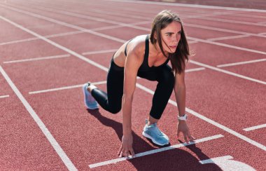 Spor giyimde motive olmuş genç bir kadın koşucu açık havada koşmaya hazırlanıyor.
