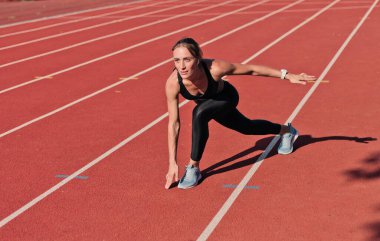 Spor giysili formalı bir kadın stadyumda koşmadan önce ısınma antrenmanı yapıyor.