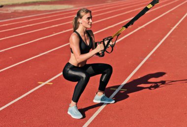 Güçlü, zayıf bir kadın, güneşli bir günde spor yaparken stadyumun raylarında spor yapıyor.