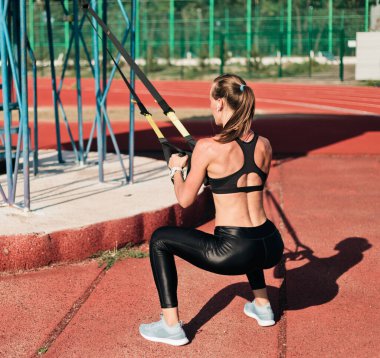 Güçlü, zayıf bir kadın, güneşli bir günde spor yaparken stadyumun raylarında spor yapıyor.