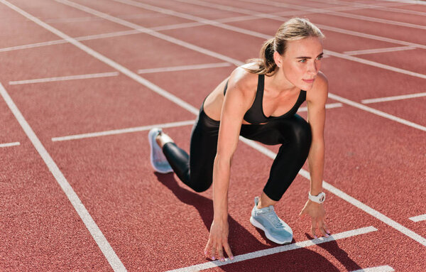 Young motivated woman runner in sportwear getting ready to run sprint at low start outdoor