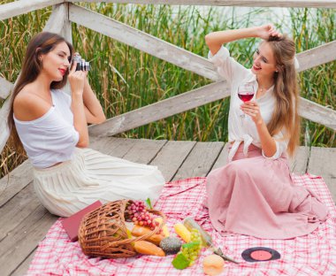 İki neşeli genç kadın yaz günü dışarıda piknik yapıyorlar. Eski moda elbiseli iki kız arkadaş göl kıyısında birlikte vakit geçiriyorlar..