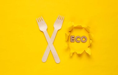 Sarı arka planda çevre dostu ahşap çatallar. Yırtık kağıt üzerinde kelime eko. Minimalizm. Üst görünüm
