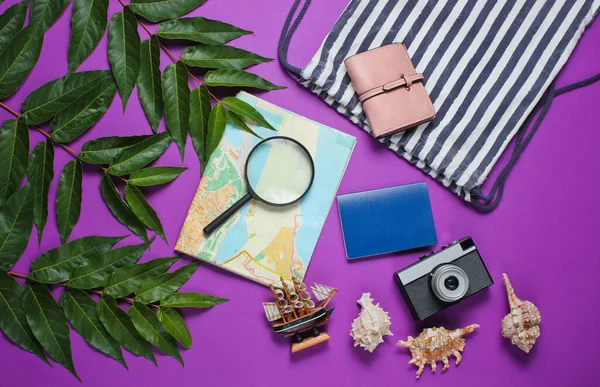 Minimalistic travel still life flat lay style. Tourist traveler accessories on purple background with tropical leaves. Top view