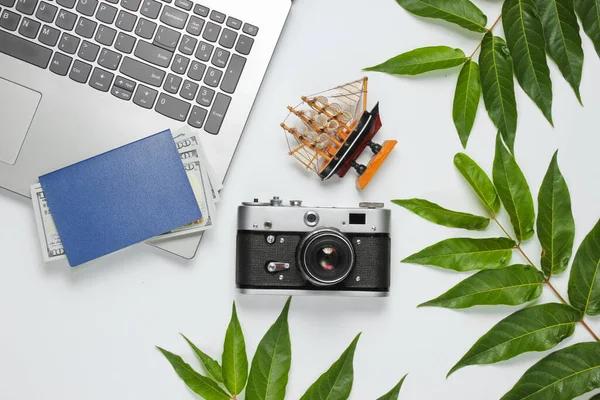 Minimalistic travel still life flat barking style. Tourist traveler accessories, laptop on white background with tropical  leaves. Top view