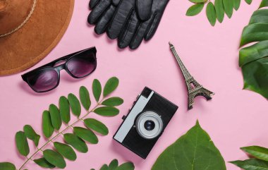 Jorney 'den Paris' e. Kadın aksesuarları, retro kamera, yeşil yapraklı pembe pastel arka planda Eyfel kulesinin biblosu. Üst görünüm
