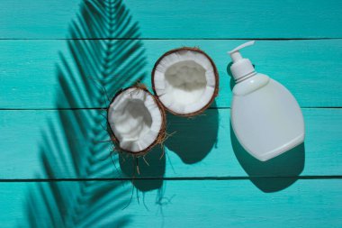 Minimalist güzellik hala hayattadır. İki parça doğranmış hindistan cevizi ve mavi ahşap arka planda palmiye yapraklarından gölgeli beyaz krema. Yaratıcı moda konsepti. Üst görünüm.