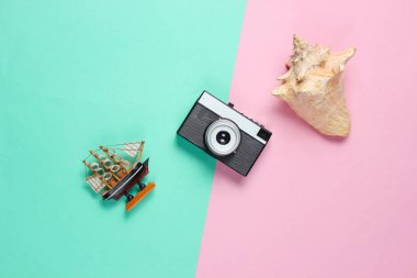 Minimalist seyahat hala hayattadır. Deniz kabukları, retro kamera, dekoratif gemi mavisi pembe pastel arka plan. Üst görünüm