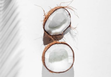 Minimalist tropikal natürmort. Beyaz arka planda palmiye yapraklarının gölgeleriyle hindistan cevizi yarıları. Yaratıcı moda konsepti. Üst görünüm.