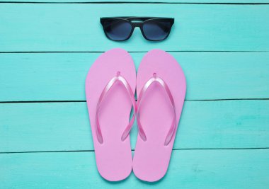 Tropik plaj yaşam tarzı. Mavi ahşap arka planda terlik ve güneş gözlüğü. Yaz dönemi. Üst görünüm