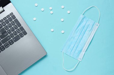 Tıbbi geçmişi var. Modern bir doktorun çalışma alanı. Laptop, haplar, mavi arka planda gazlı bez maskesi. Üst Manzara. Düz yatıyordu