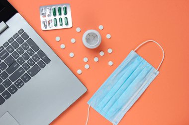 Tıbbi geçmişi var. Modern bir doktorun çalışma alanı. Laptop, haplar, şeftali rengi arka planda gazlı bez maskesi. Üst Manzara. Düz yatıyordu