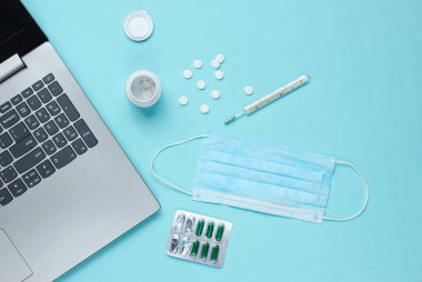 Tıbbi geçmişi var. Modern bir doktorun çalışma alanı. Laptop, haplar, gazlı bez maskesi, mavi arka planda termometre. Üst Manzara. Düz yatıyordu