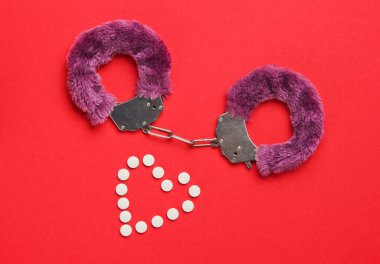 Seks dürtüsü. Kırmızı arka planda seks oyunları için haplı kelepçe (form kalp). Cinsel bdsm oyuncağı. Aşk, erotik kavram. Üst görünüm