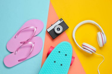 Hippi kıyafeti. Kulaklıklı kaykay, parmak arası terlik, renkli arka planda retro kamera. Yaratıcı moda minimalizmi. Eski moda 80 'ler tarzı. Asgari yaz eğlencesi. Müzik konsepti. Üst görünüm