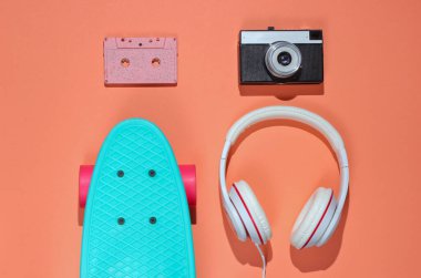 Hippi kıyafeti. Kulaklıklı kaykay, mercan rengi arka planda ses kaseti. Yaratıcı moda minimalizmi. Eski moda 80 'ler tarzı. Asgari yaz eğlencesi. Müzik konsepti. Üst görünüm