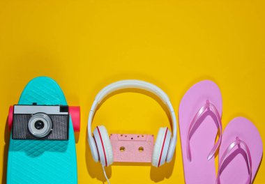 Hippi kıyafeti. Kaykay, ses kaseti, kulaklıklar, parmak arası terlik, sarı arka planda retro kamera. Yaratıcı moda minimalizmi. Eski moda 80 'ler tarzı. Asgari yaz eğlencesi. Müzik konsepti. Üst görünüm