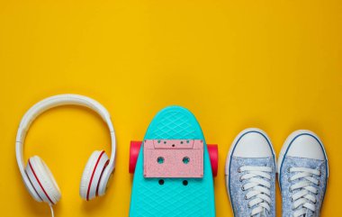 Hippi kıyafeti. Kulaklıklı kaykay, ses kaseti ve sarı arka planda spor ayakkabılar. Yaratıcı moda minimalizmi. Asgari yaz eğlencesi. Pop sanat. 80 'ler. Müzik konsepti. Üst görünüm