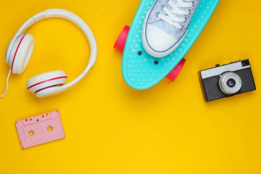 Hippi kıyafeti. Kaykay, kulaklıklar, ses kaseti, spor ayakkabıları, sarı arka planda retro kamera. Yaratıcı moda minimalizmi. Asgari yaz eğlencesi. Pop sanat. 80 'ler. Uzayı kopyala Üst görünüm
