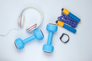 Dambıllar, akıllı bilezikler, kulaklıklar, beyaz arka planda ip atlama. Minimalist spor konsepti. Üst görünüm.