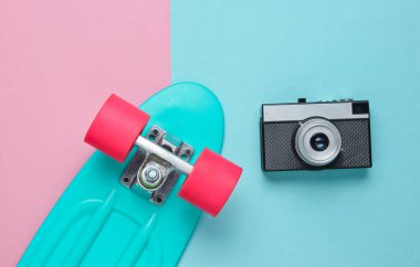 Renkli pastel arka planda kaykay ve film kamerası olan bir Retro seti. Stüdyo çekimi. Gençlik yaşam tarzı. 80 'ler. Üst görünüm