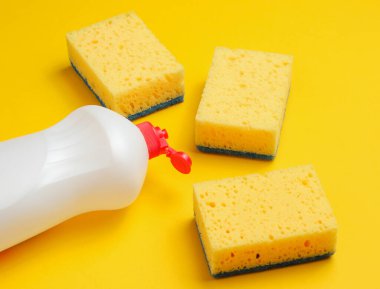 Bulaşık yıkamak için ev hanımları. Bulaşıkçı. Bir şişe kap kacak, sarı arka planda süngerler..