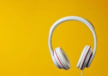 Beyaz klasik kulaklıklar sarı arka planda izole edilmiş. Retro tarzı. Minimalist müzik konsepti.