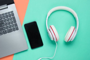 Modern dijital cihazlar ve aksesuarlar. Laptop, akıllı telefon, renkli arka planda kulaklık. Pastel renk eğilimi. Üst görünüm. 